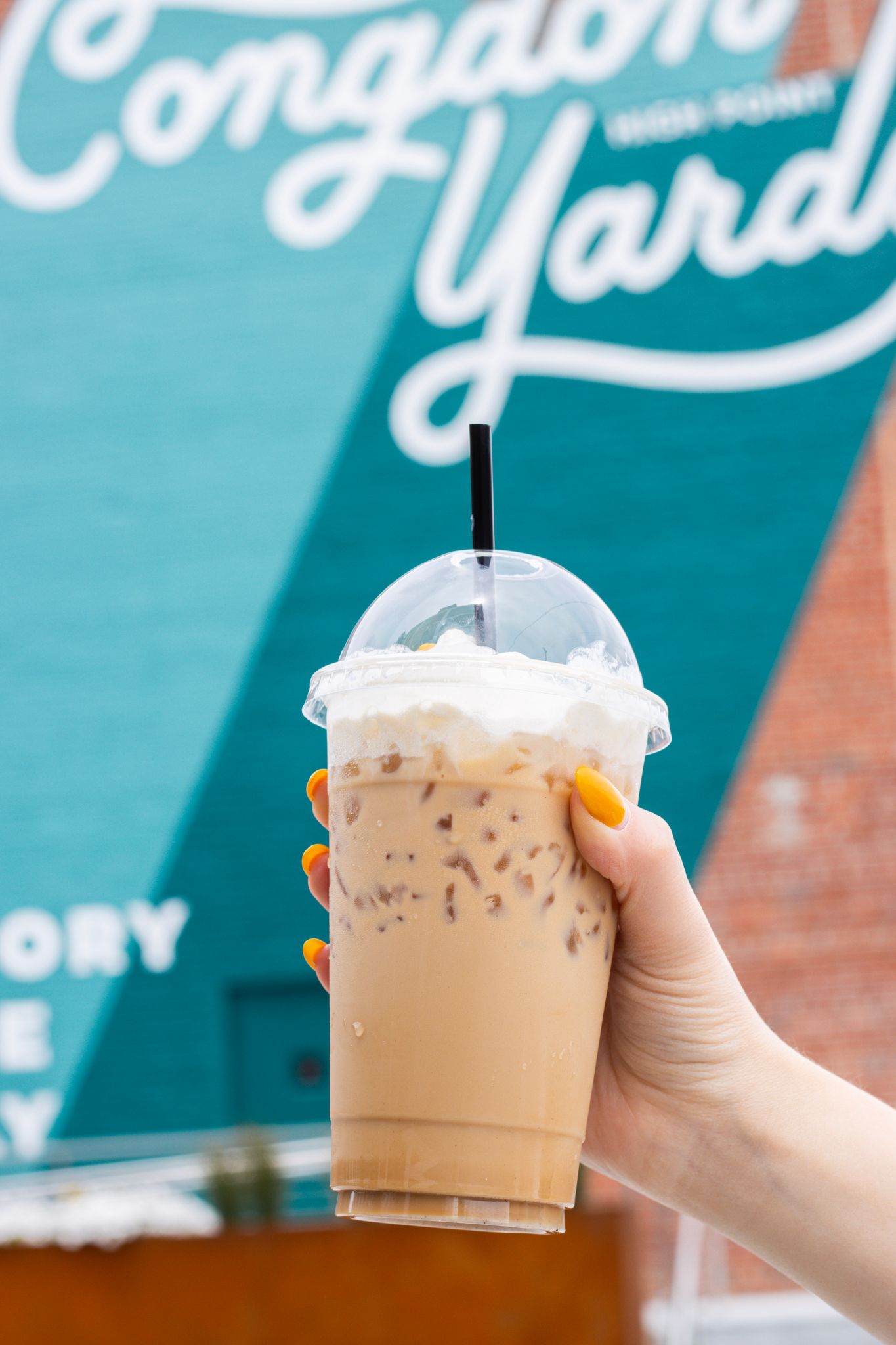 An iced coffee from Lil's Coffee Bar in High Point, NC held up in front of the Congdon Yards mural.