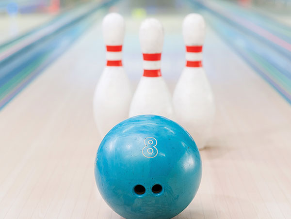 A bowling ball about to hit three white pins. 