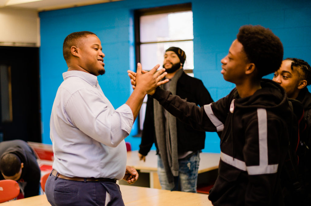 Cyril Jefferson and a student perform a handshake in a classroom.