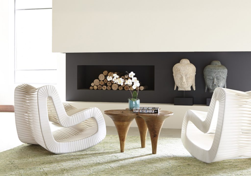 Two modern white chairs sit on either side of a wooden coffee table in front of a modern, gray fireplace.