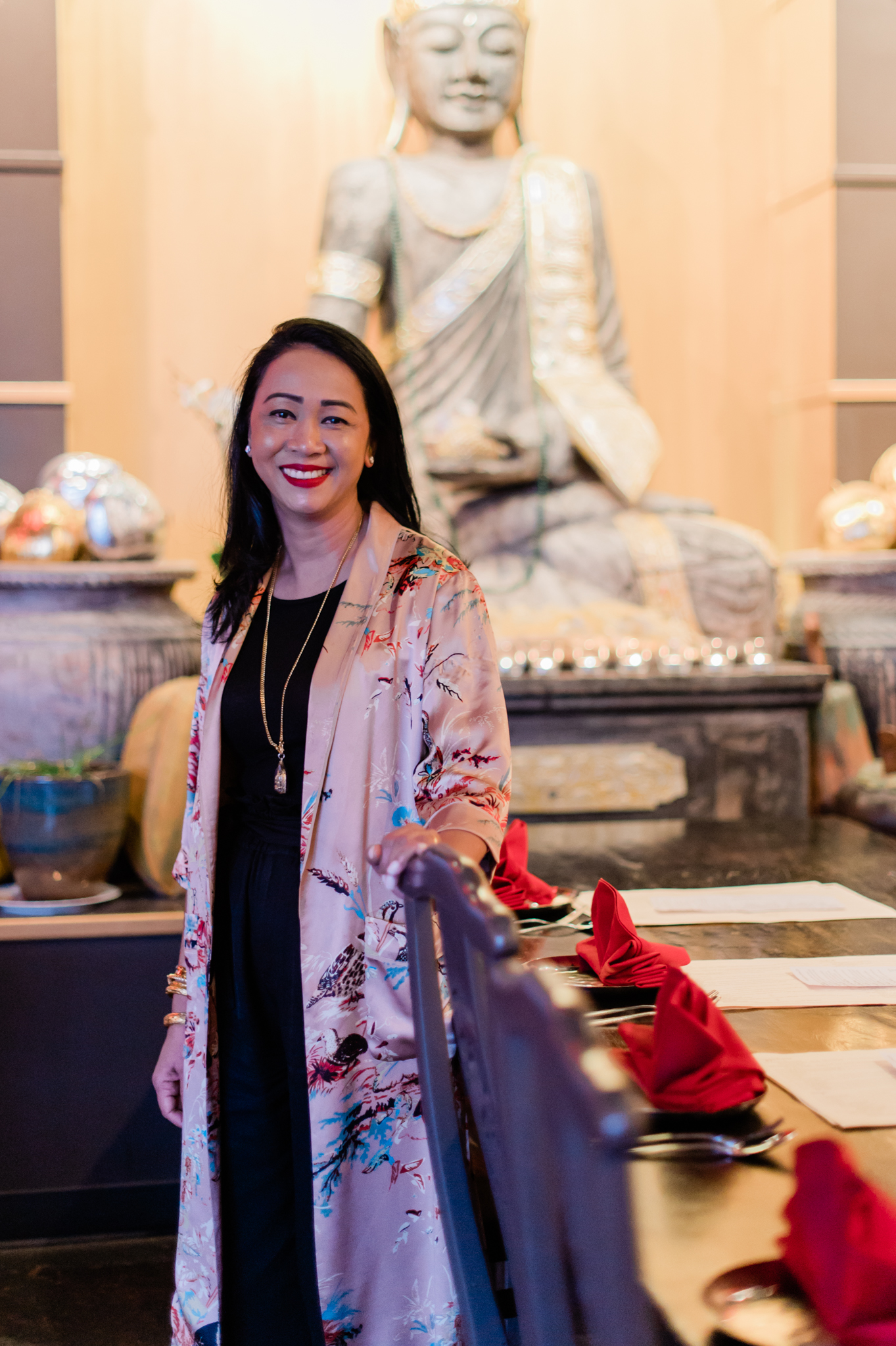 Tu Sen, owner of 98 Asian Bistro, wears a silk kimono over a black dress, and stands in the restaurant in front of a Buddha statue.