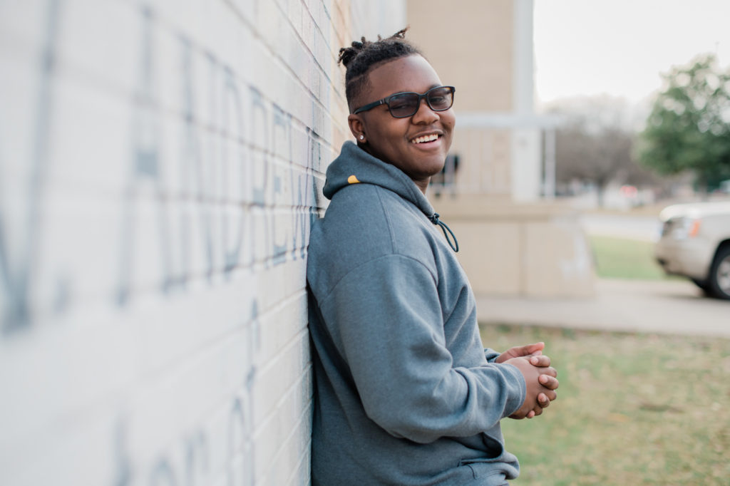 Isaiah Tatum, a student in High Point at T. W. Andrews High School leans on a wall, smiling.