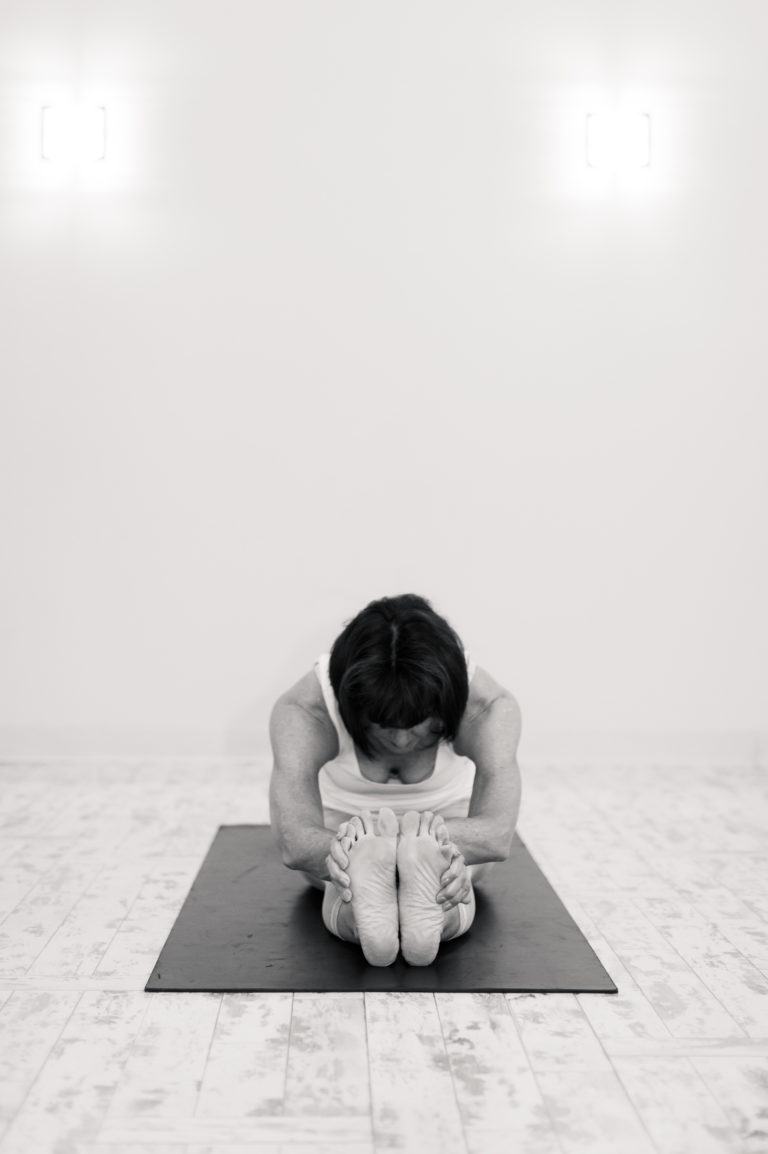 A woman at Yoga and Wellness of High Point sits on a yoga mat stretching.
