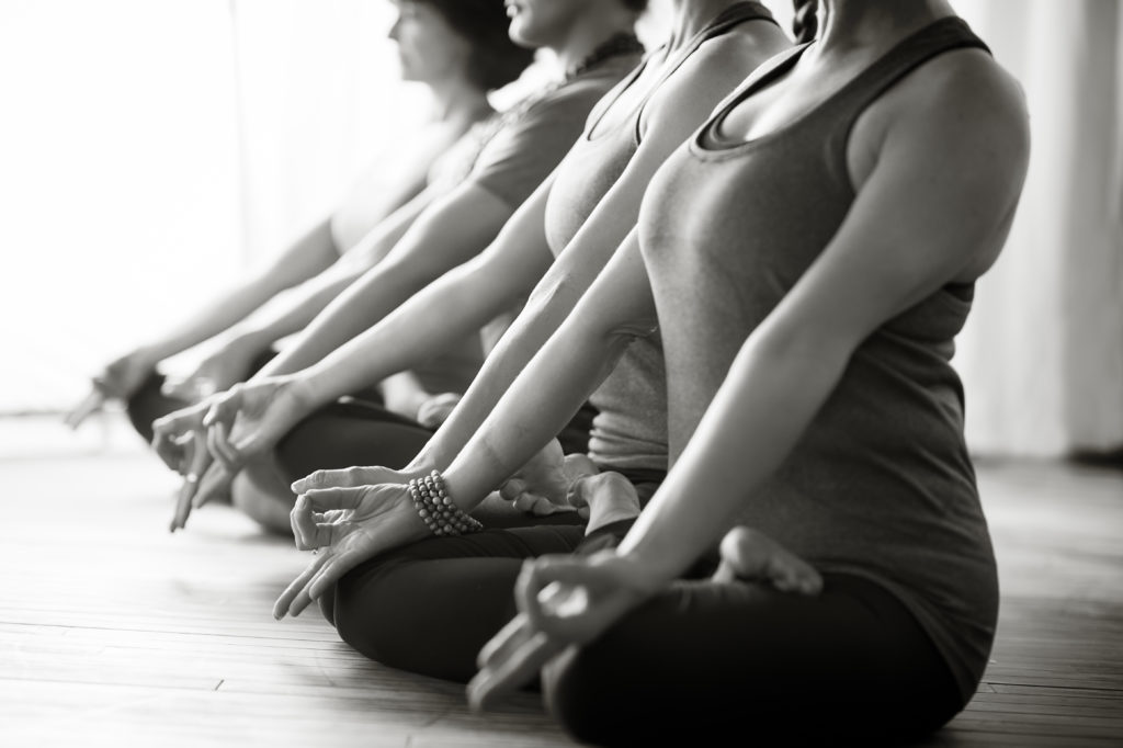 A row of women sit cross legged, meditating at Pure Light Yoga.