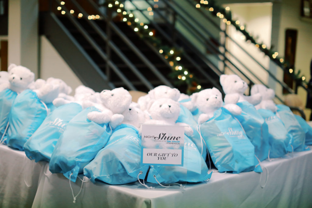 White teddy bears are in blue bags laying on a table with "Night to Shine" cards on it.