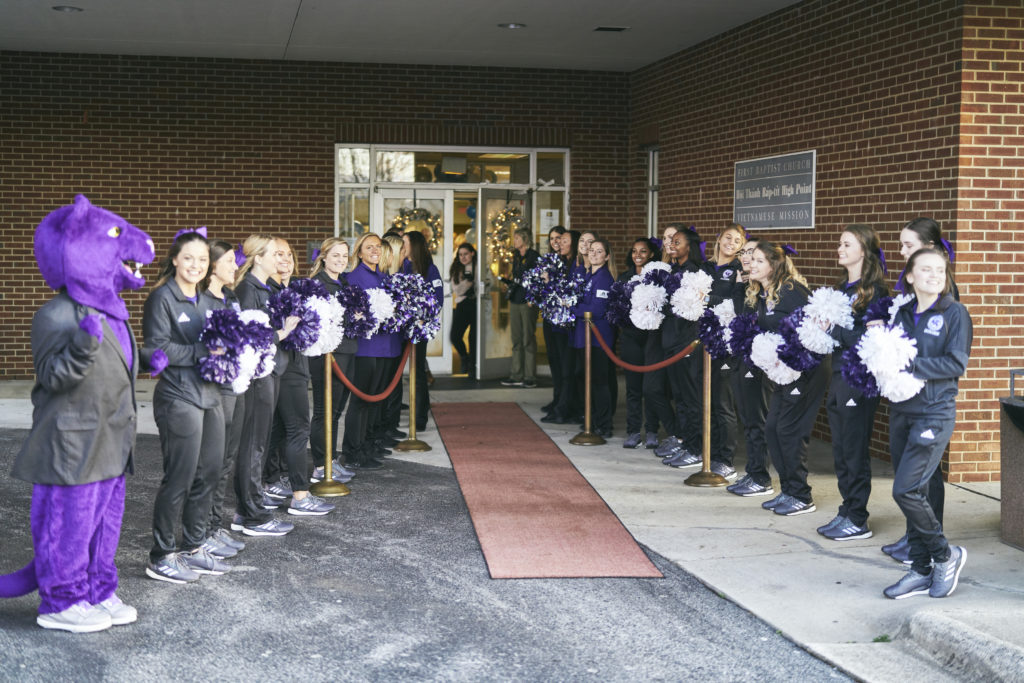 High Point University cheerleaders and mascot line a red carpet outside.
