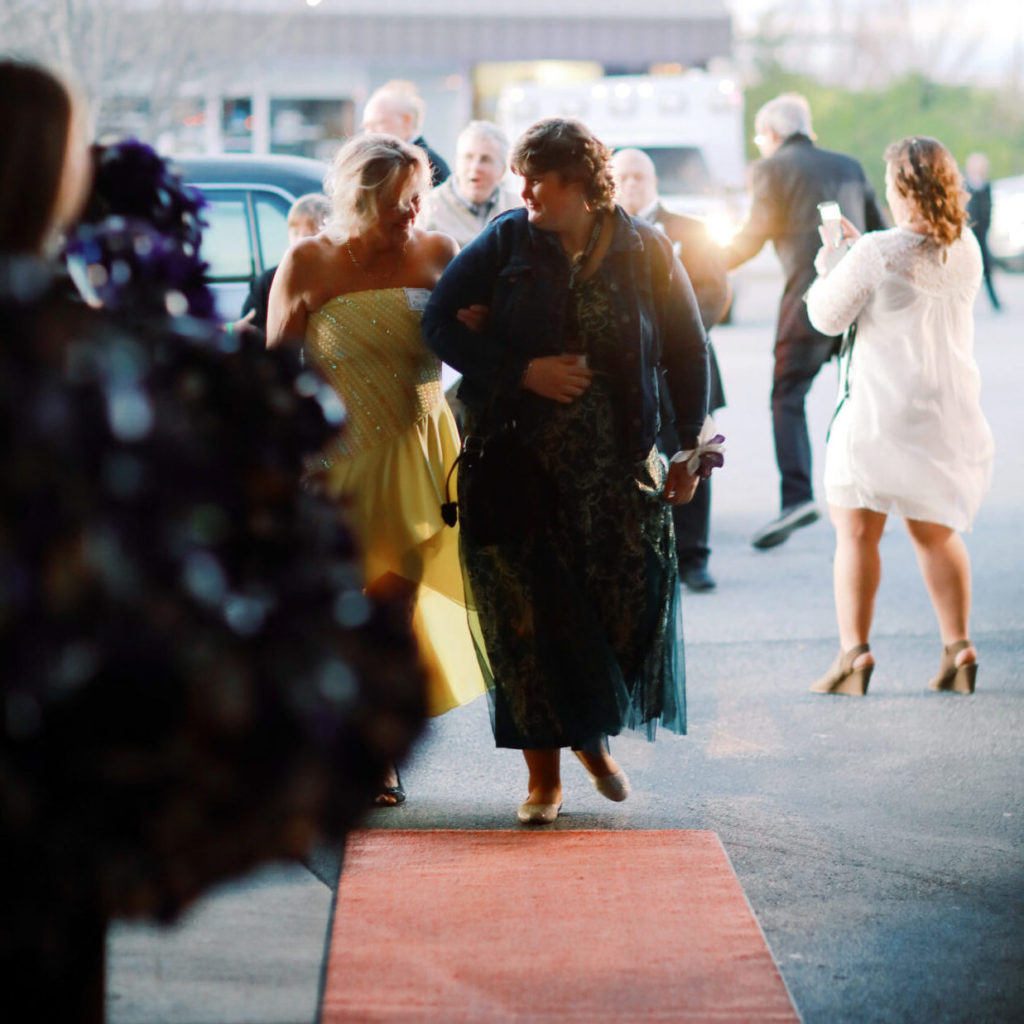Two women dressed up walk arm in arm down a red carpet of a Night to Remember dance in High Point, NC .