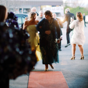 Two women dressed up walk arm in arm down a red carpet of a Night to Shine dance in High Point, NC .