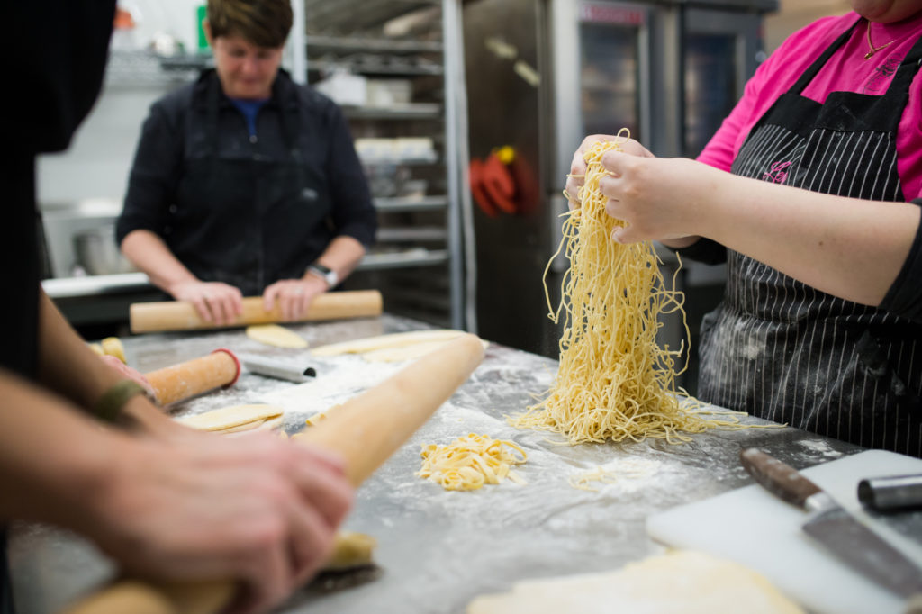 A shot of hands kneading pasta dough on an industrial kitchen counter.