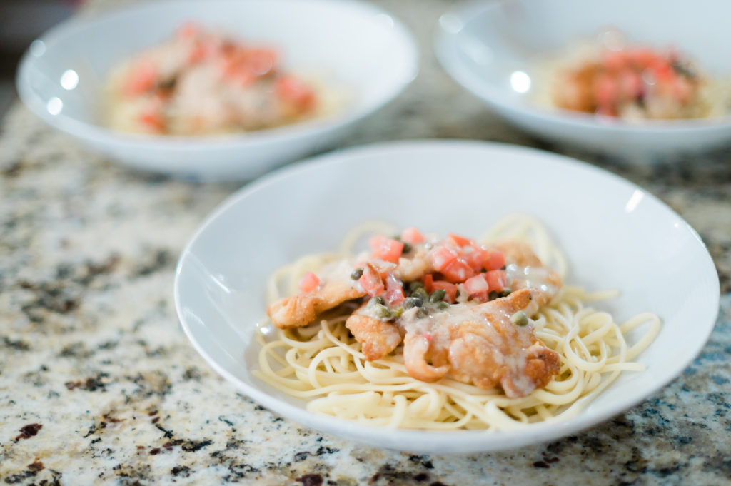 Several plates of shrimp pasta sit on a marble counter.