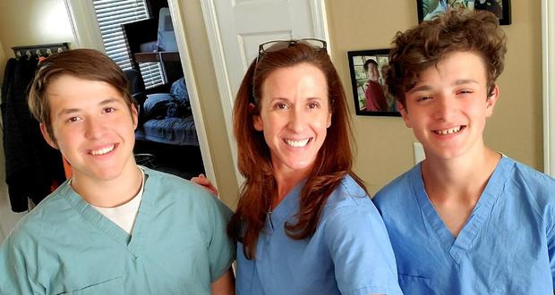 Bevin Strickland smiles at camera wearing scrubs, standing between her two sons.