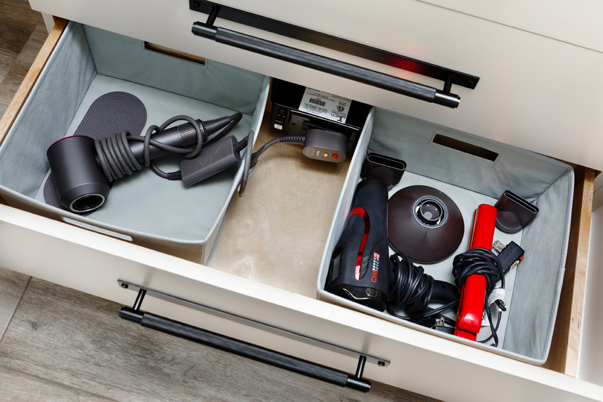 An open counter drawer with a blow dryer and several other hair tools.