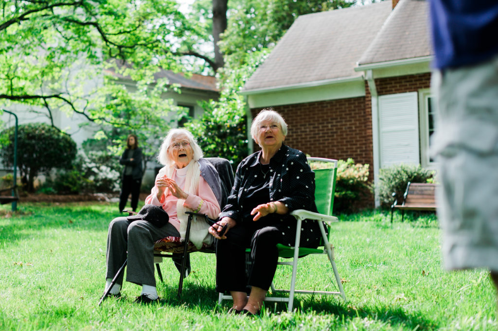 Jean and her daughter sit in camp chairs, smiling up at someone standing nearby.