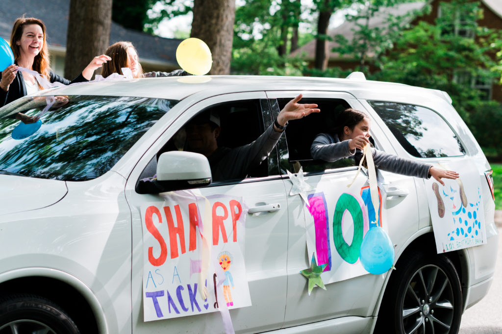 People wave out of a car with signs that say "Sharp as a Tack" and "101" on the side of the car. 