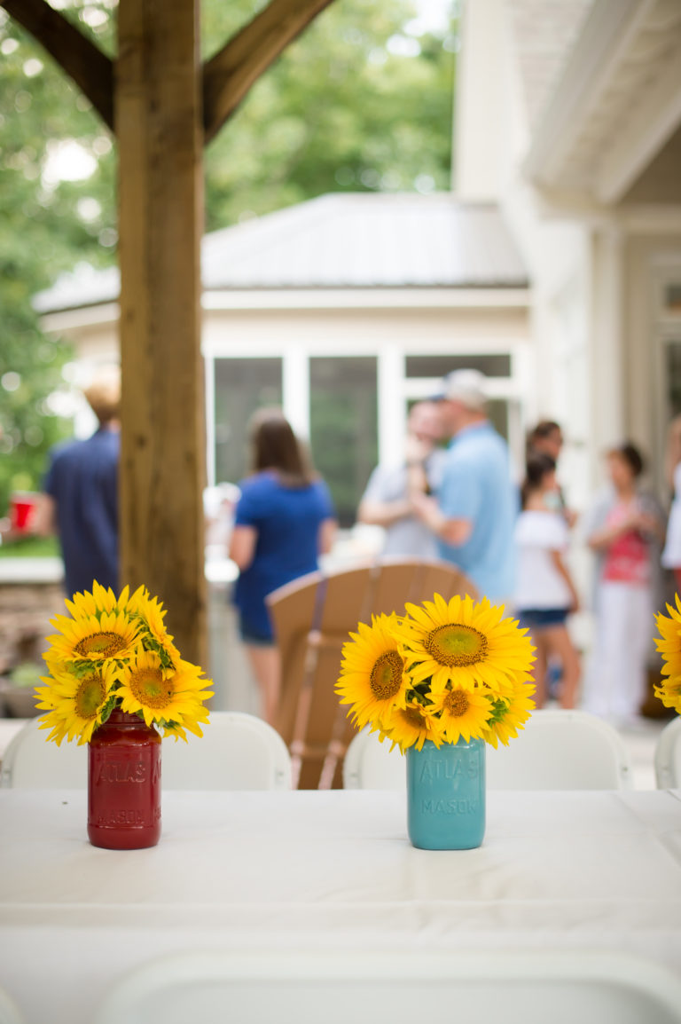 Vases of sunflowers sit on a table with people in the background.