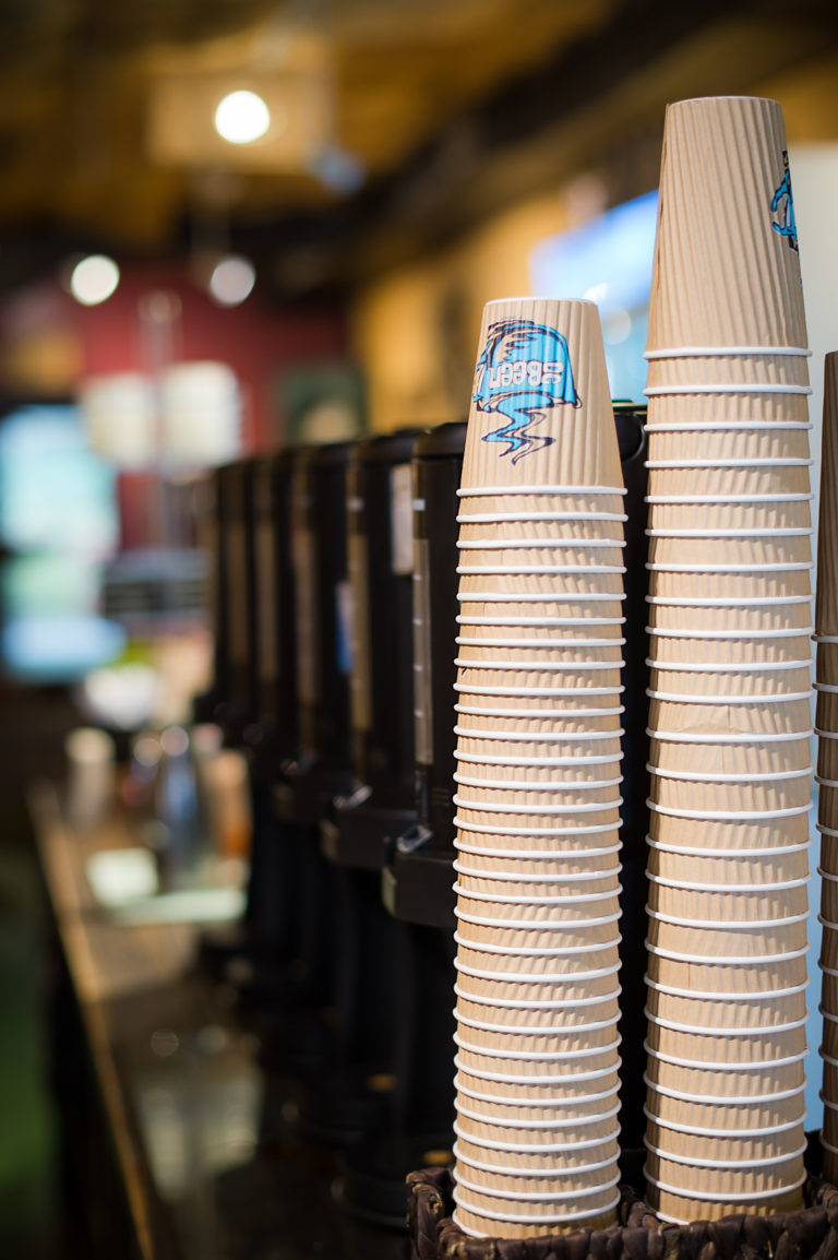 A stack of DeBeen Espresso coffee cups stand in front of the drip coffee machines.