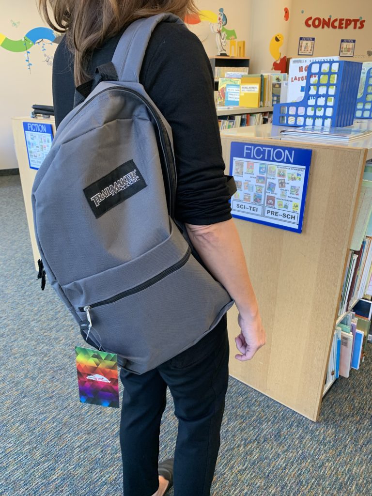 A woman stands wearing one of the giveaway backpacks in the High Point Public Library.