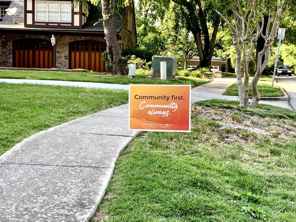 A yard sign that says "Community First. Community Always." sits in the grass.