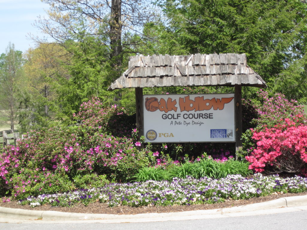 A sign sits among flowers and shrubs that reads, "Oak Hollow Golf Course."