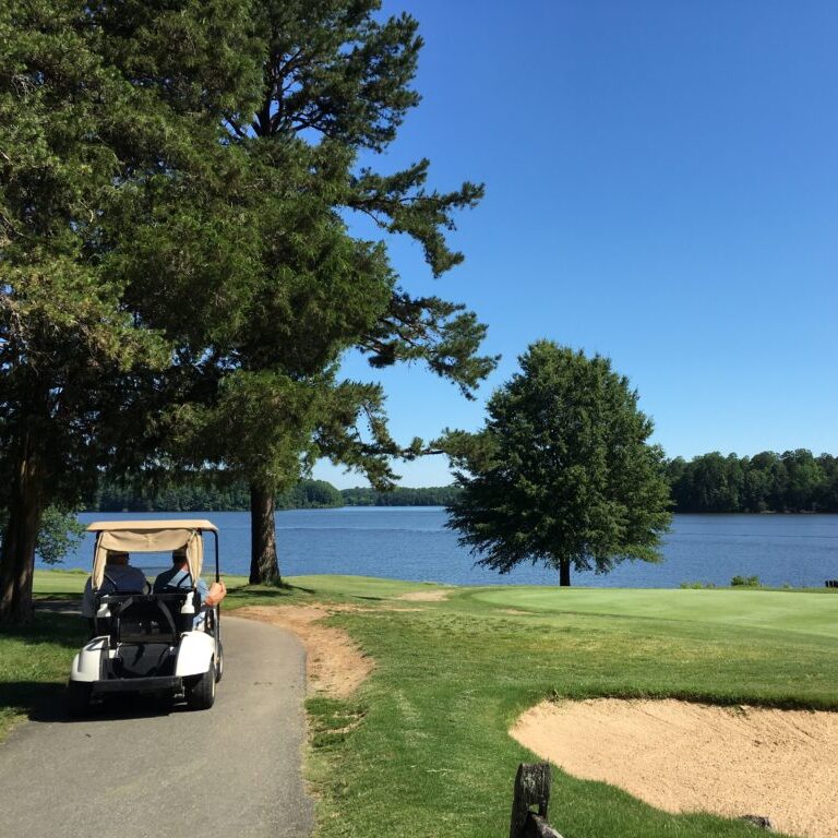 A golf cart rides along a path beside the Oak Hollow Golf Course and a sand trap.