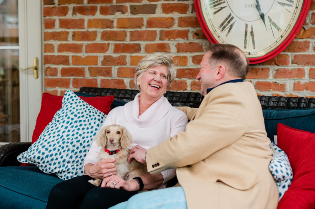 Jayne and Paul Lessard sit together on an outdoor sofa petting their dog.
