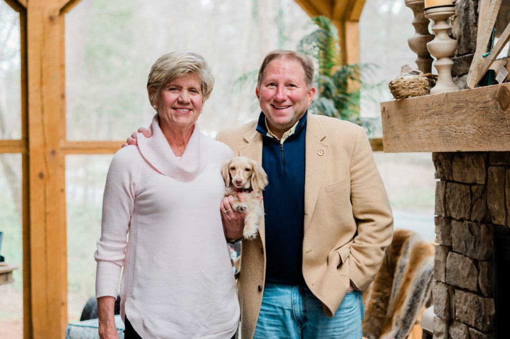 Jayne and Paul Lessard stand smiling and holding their dog.