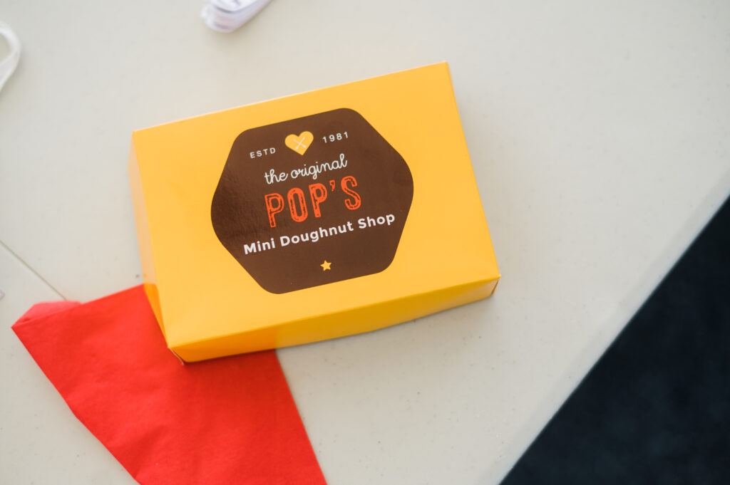 A yellow box with a logo on it that says, "Pop's Mini Doughnut Shop."