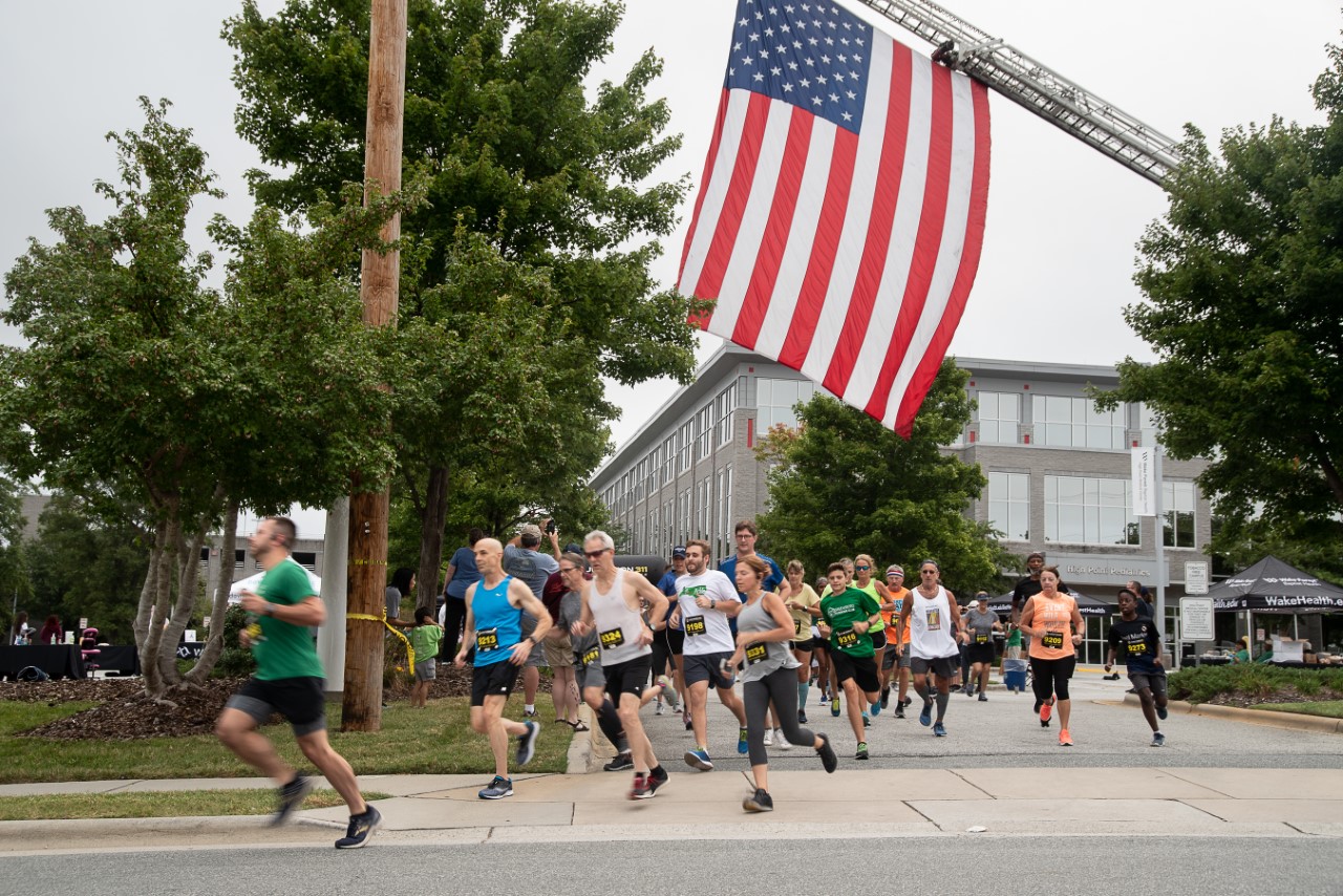 Group of runners run outside of High Point Medical Center. An American flag hangs over the runners.