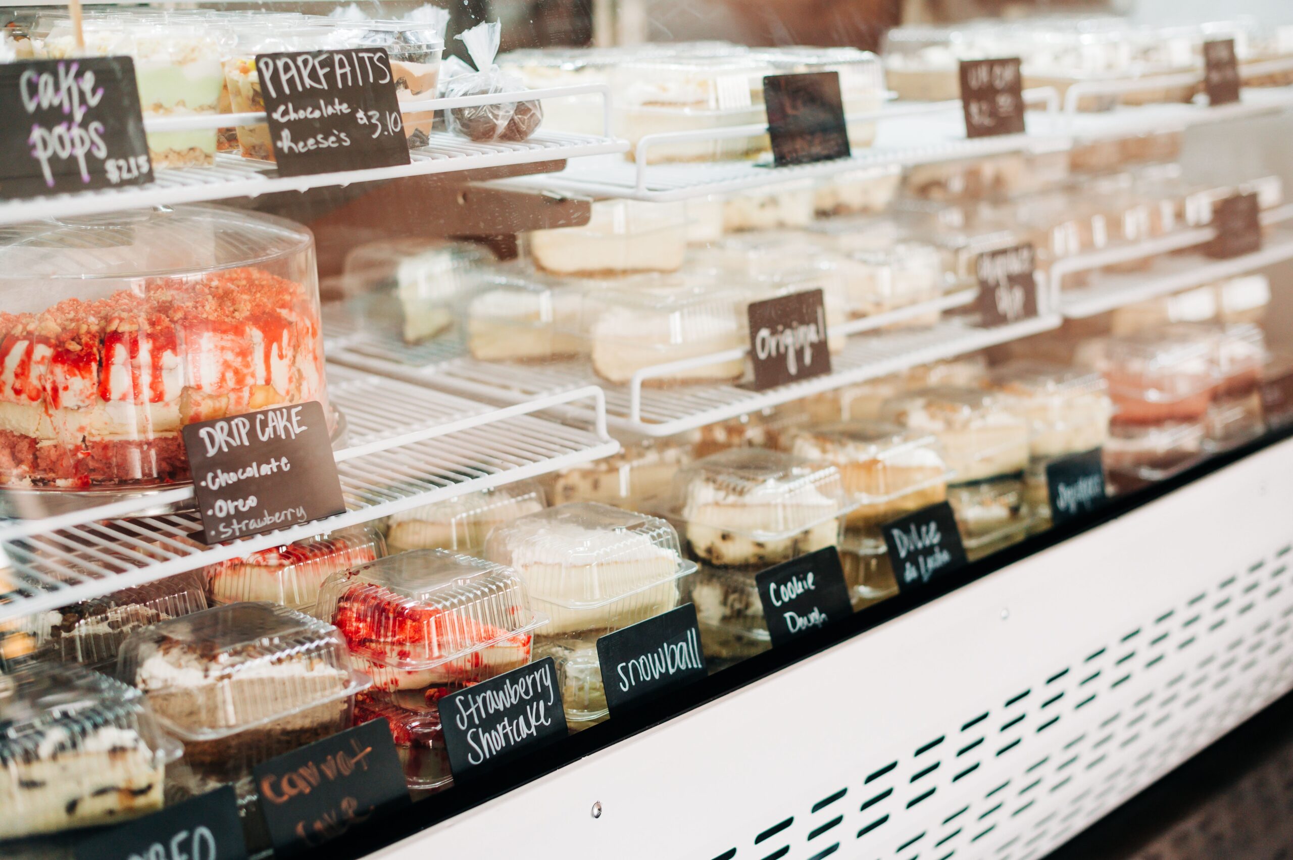 A glass bakery case with a variety of cheesecakes, cakes, and pies.