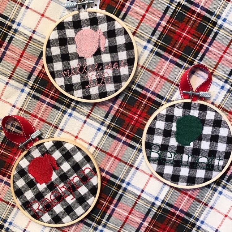 A plaid print table cloth with small embroidered hoops of children's silhouettes on buffalo plaid from Dwell and Wander Goods.