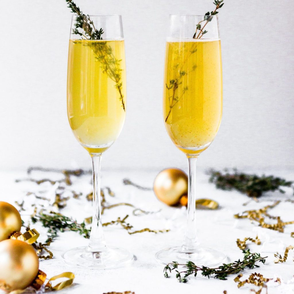 Two glasses of champagne with a spring of tyme surrounded by Christmas ornaments.