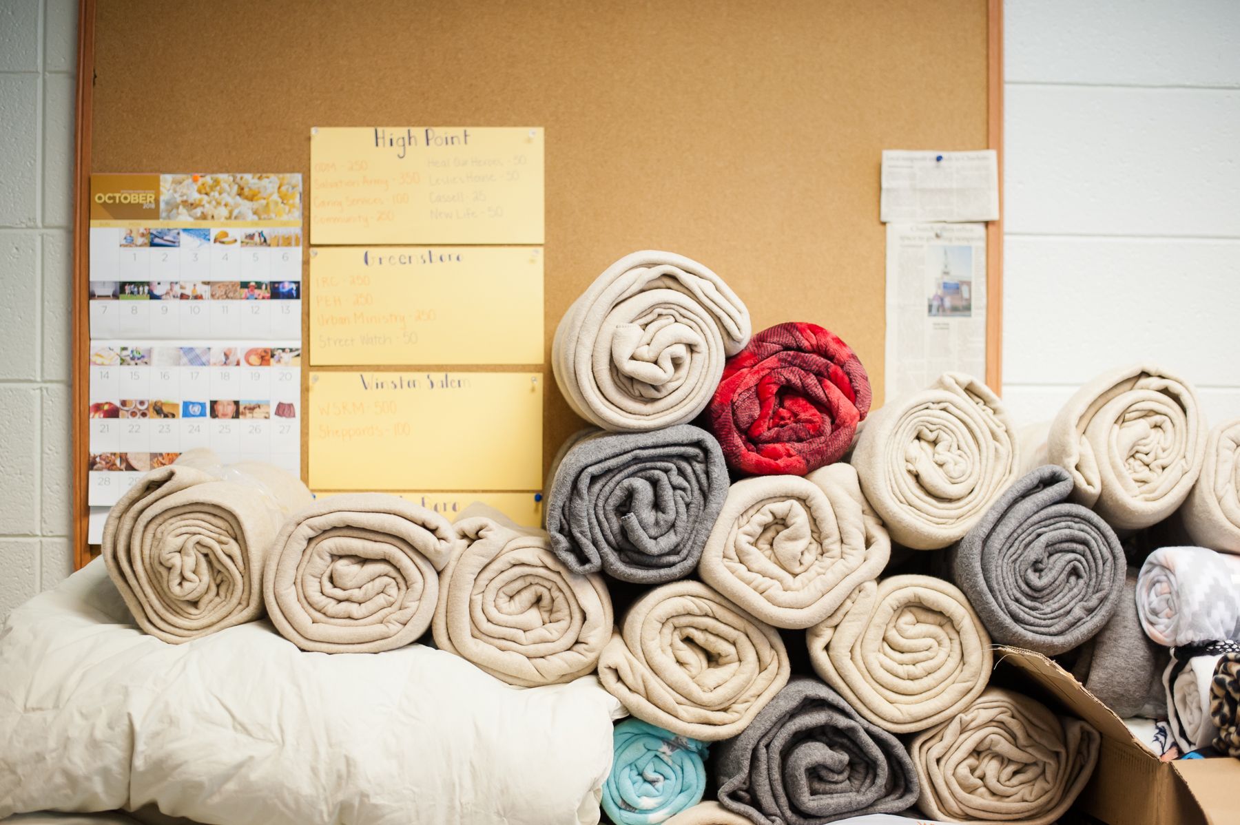 Rolls of blankets piled in front of a notice board at Cover the City Project in High Point, NC.