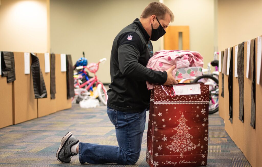 Man wears a mask and kneels beside a box of toys.