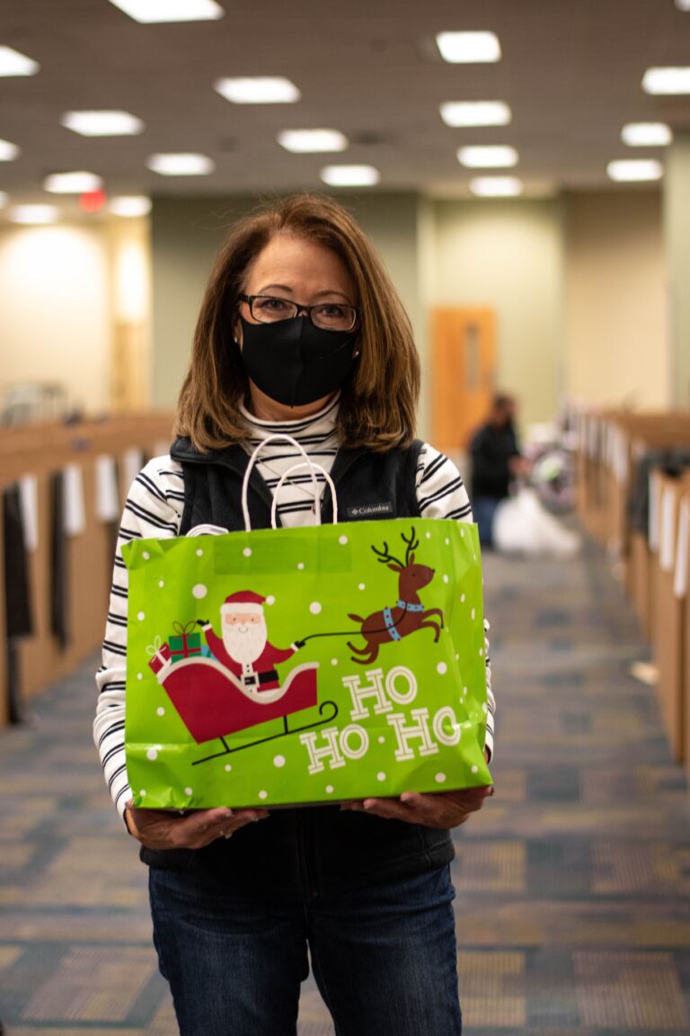 Woman wearing a mask and holding a Christmas gift bag.