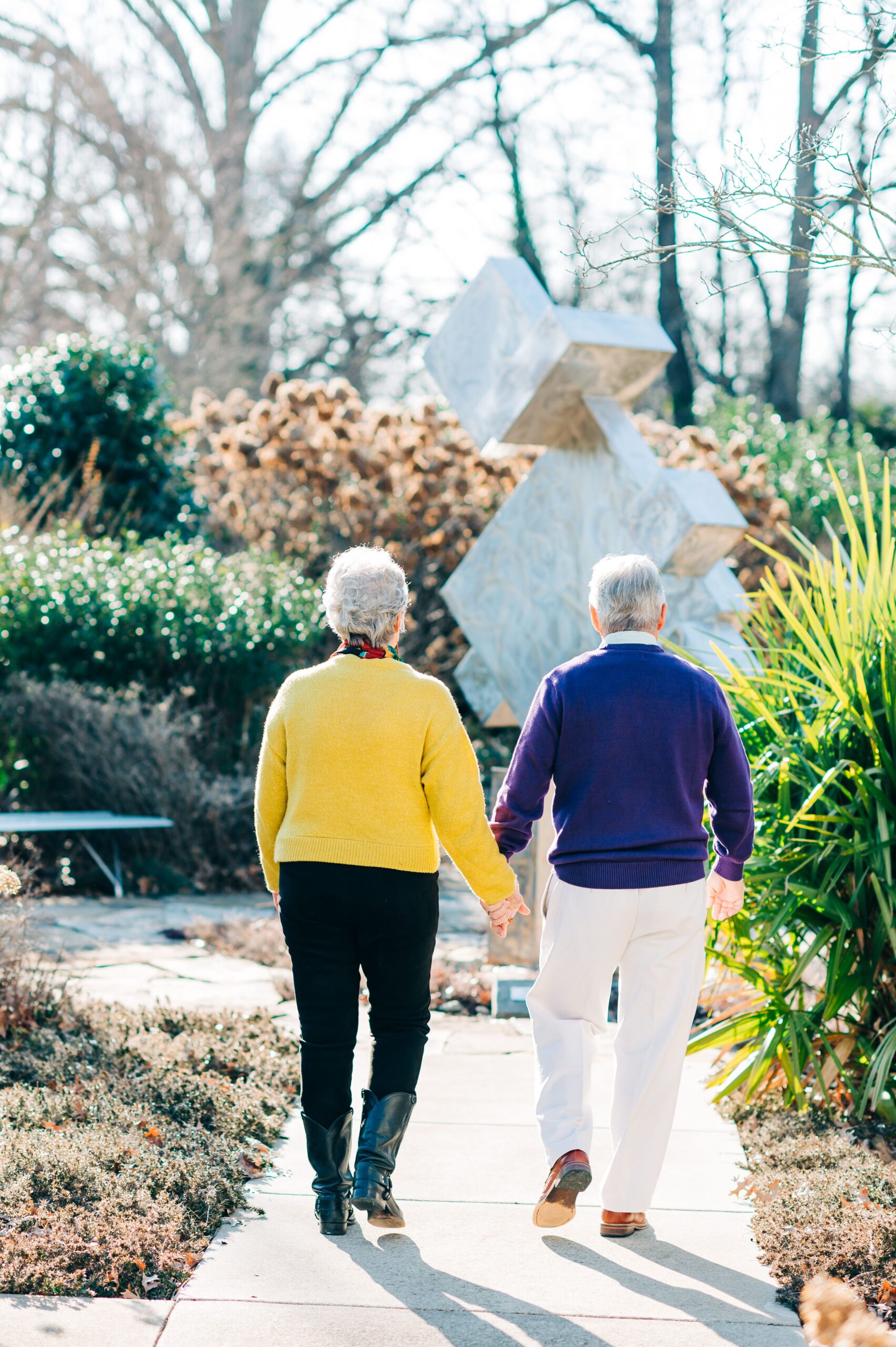 Abby and David Williams walk with their back to the camera, holding hands, as they walk through the Bienenstock Library gardens.