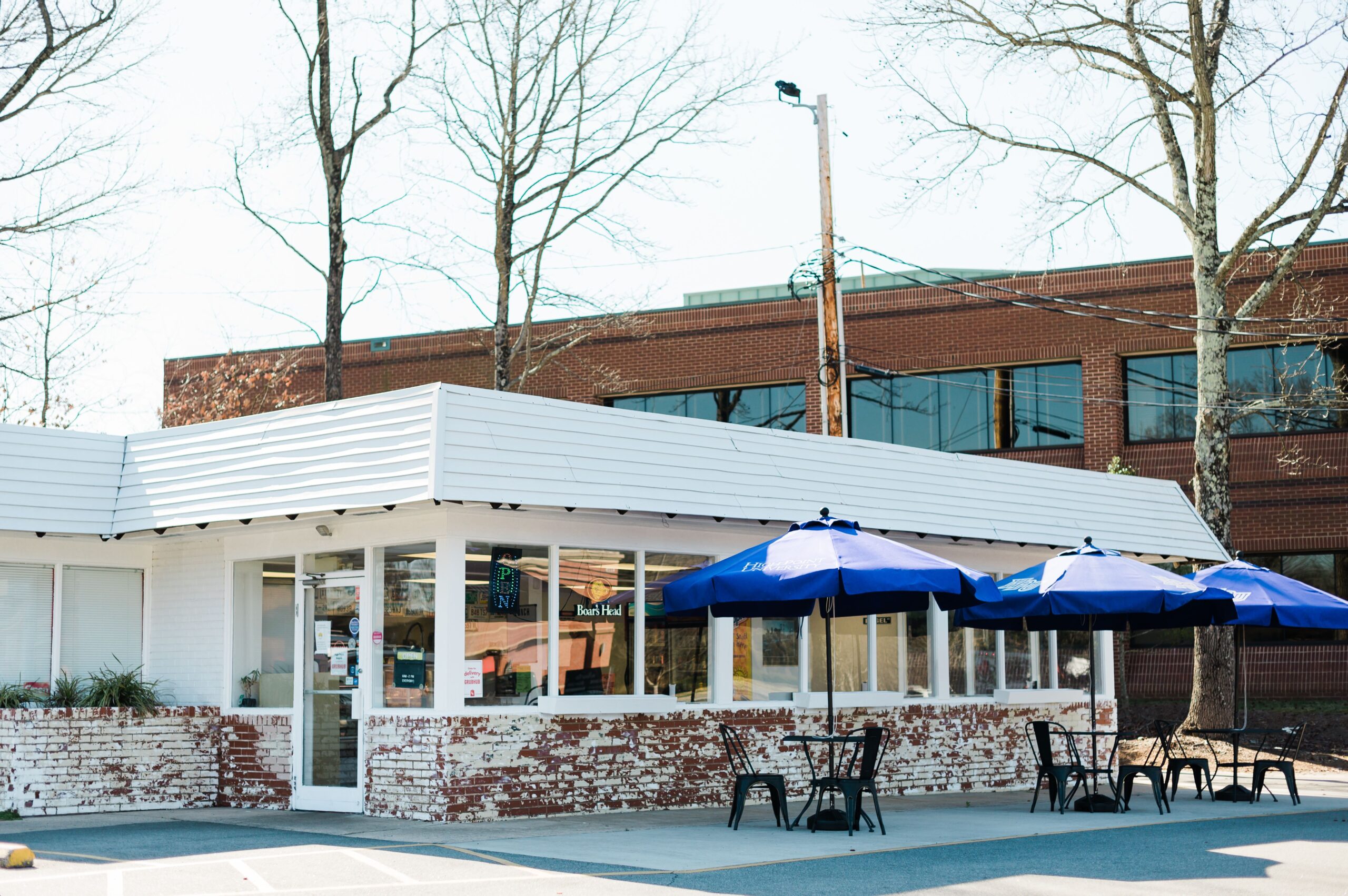 The exterior of High Point Bagels in High Point, NC, with patio tables with High Point University umbrellas.