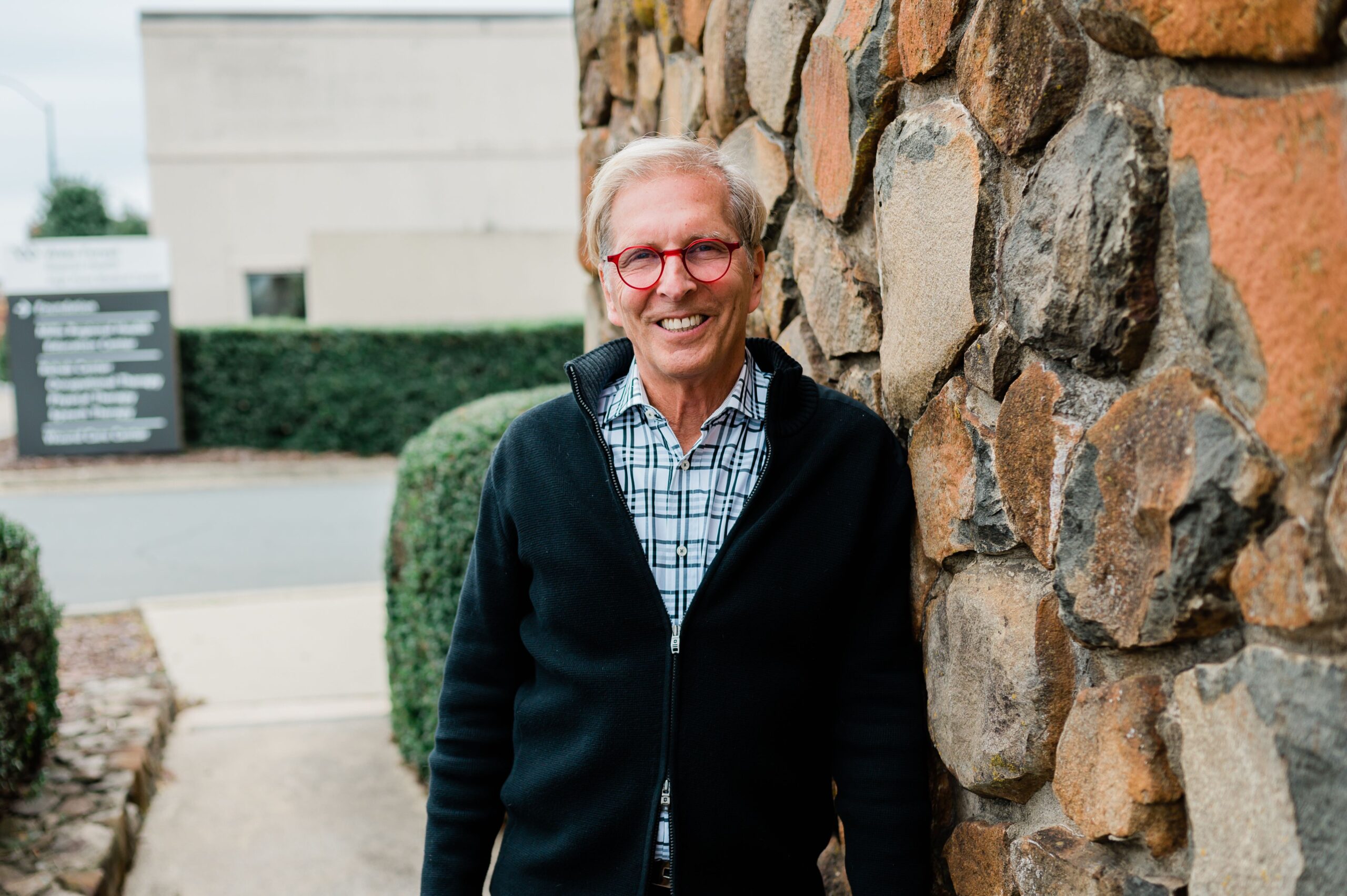 Dr. Frosty Culp, retired dentist from High Point, NC smiles at the camera while leaning on a wall at the Community Clinic of High Point.