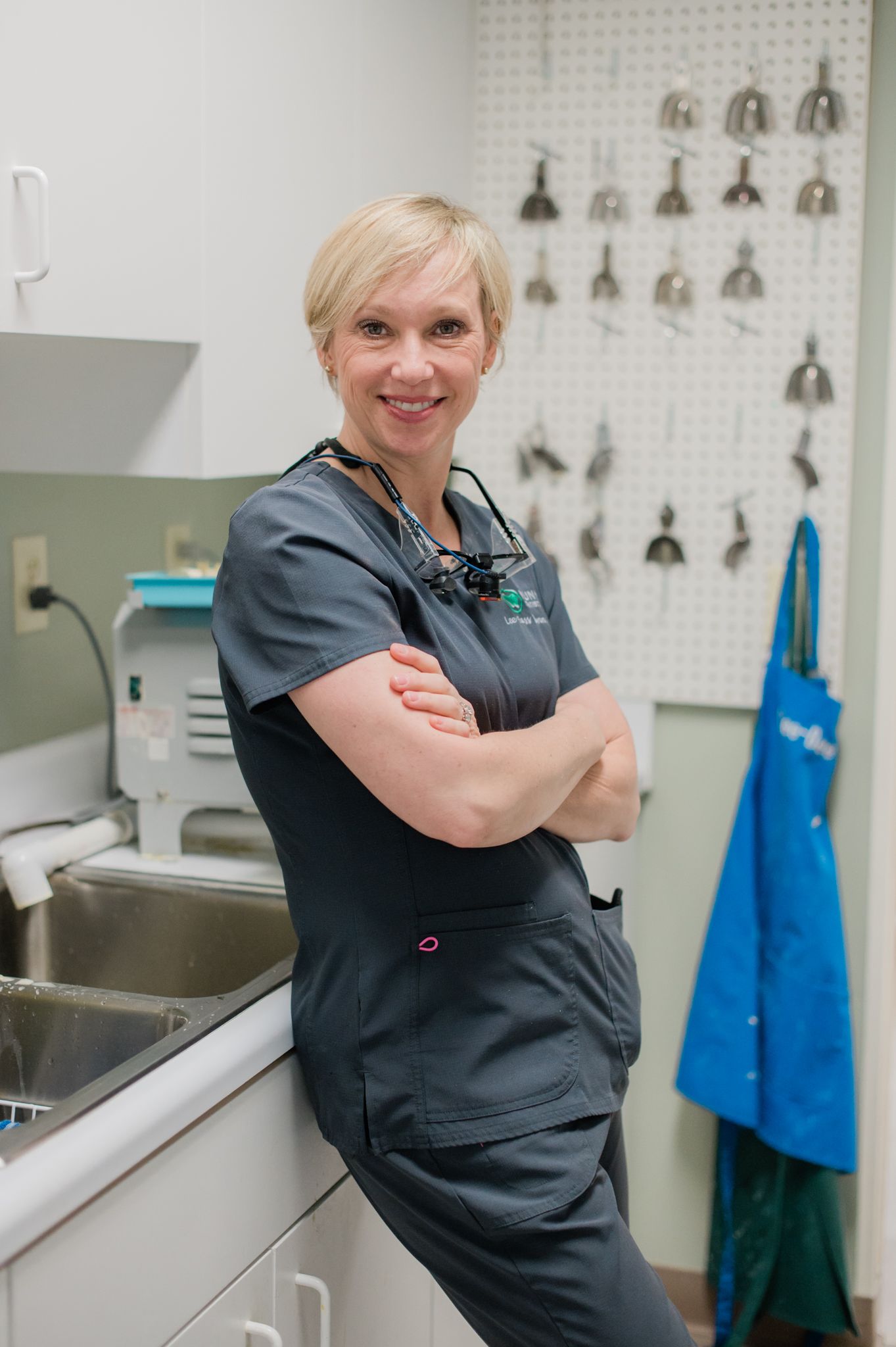 Dr. Lee Bass Nunn, dentist at Nunn Dentistry in High Point, NC wears scrubs and leans on the counter in her office. 