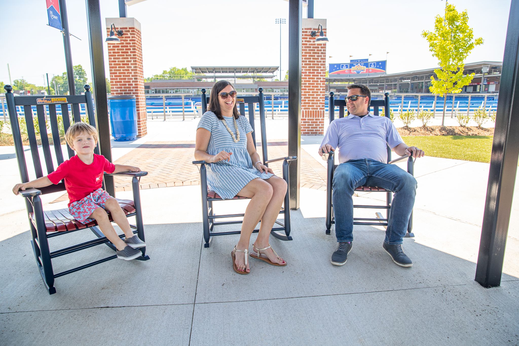 A man, woman, and child sit in rocking chairs at the High Point Rockers Stadium at Blessing Park. The park offers things to do in High Point, NC for families.