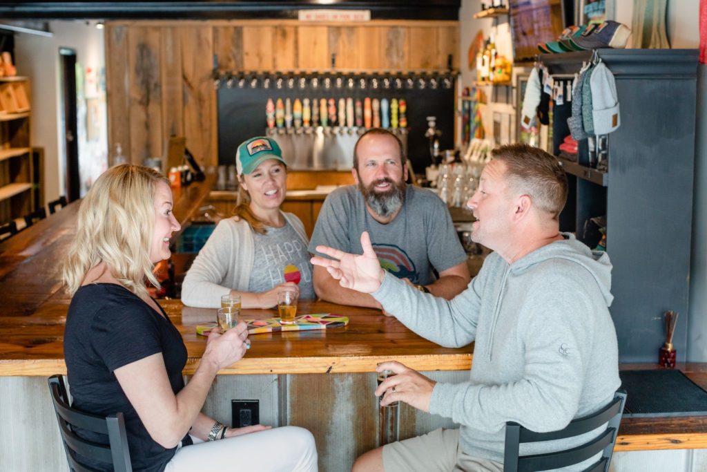 A couple sits at the bar at Goofy Foot Taproom in High Point, NC chatting with owners, Jeff and Tiffany Thompson.
