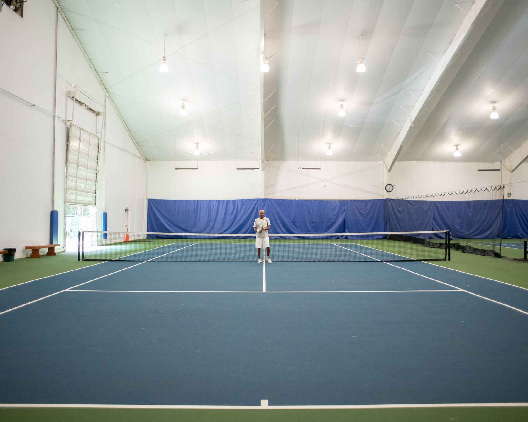 Junius Chatman, tennis director at Oak Hollow Tennis Center in High Point, NC, stands far away on indoor court.