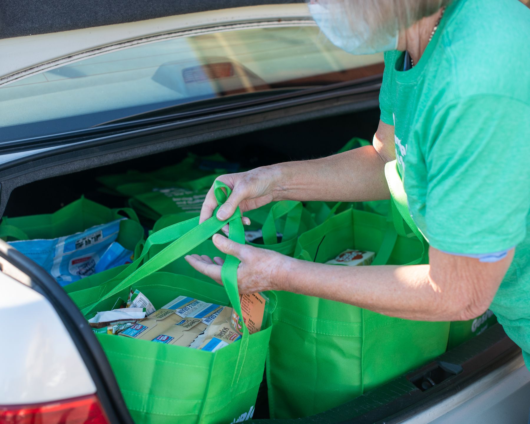 A woman loads grocery bags for A Simple Gesture High Point into her car trunk.