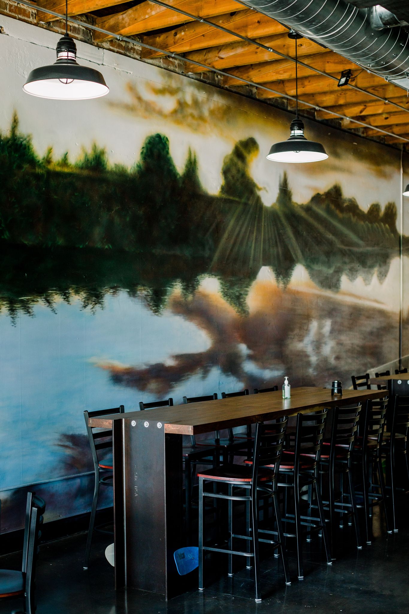 A mural on the back wall of Paddled South Brewing Co. in High Point, NC is behind long friendship tables.