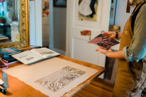 Annabella Boatwright, owner of Neon Tumbleweed Studio in High Point, NC lifts up one of her stamps from a piece of fabric
