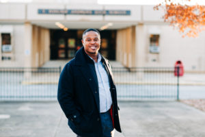 Cyril Jefferson of Change Often stands smiling in a jacket in front of T. Wingate Andrews High School in High Point, NC