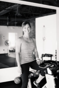 Lori Teppara smiles at the camera, sitting on a bike in FIT HUB in High Point, NC.