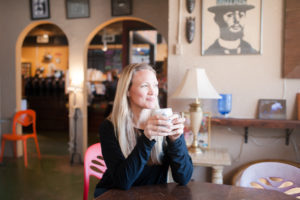 Debeen Owner Debbie Maier sips coffee and looks off into the distance in her High Point, NC coffee shop.