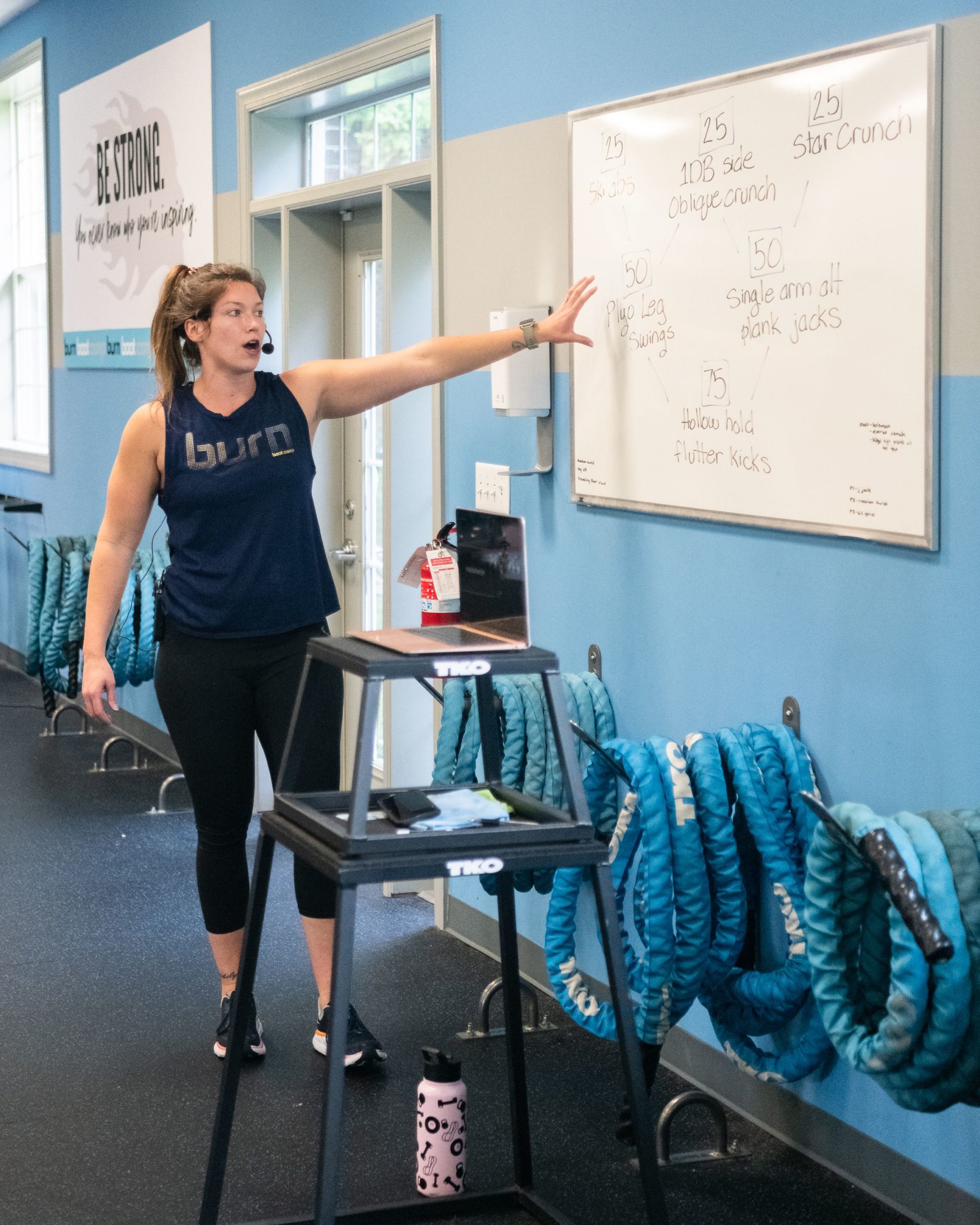 A personal trainer at Burn Boot Camp in High Point points to a white board with reps.
