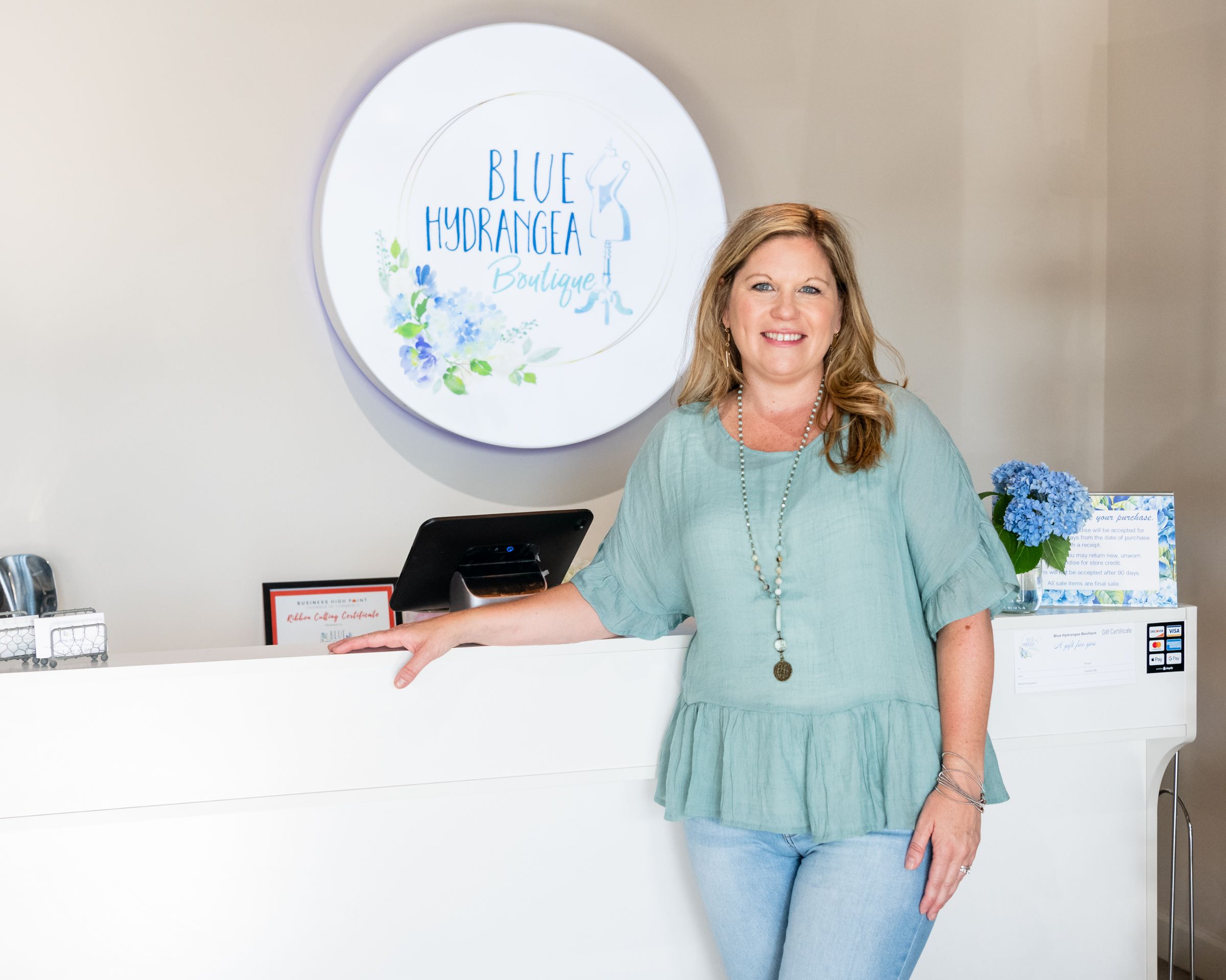 Elissa Porter, owner of Blue Hydrangea Boutique stands in front of her sign in her store in High Point, NC.