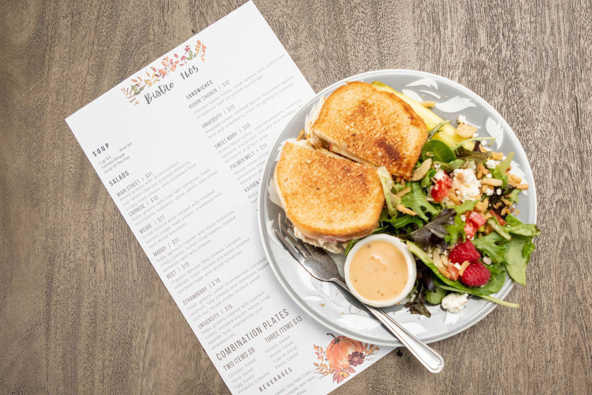 A menu from Bistro 1605 lays on a table with a sandwich and salad from a restaurant where to eat in High Point, NC.